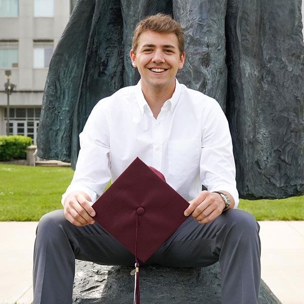 William Borders sitting down and holding a maroon mortarboard.