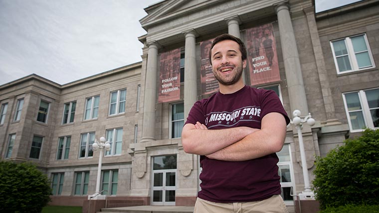 A student in a maroon Missouri State t-shirt posing in front of Carrington Hall.