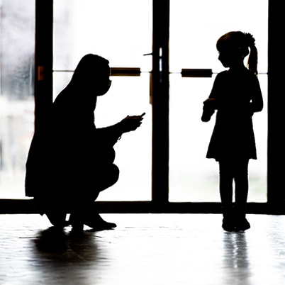 Shadow image of an adult kneeling to speak with a child.