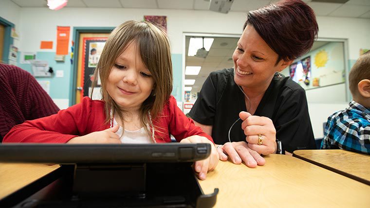 Teacher helping student through course work on tablet.