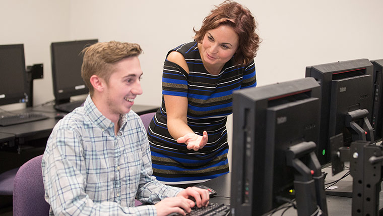 A teacher talking to a student at a computer station.