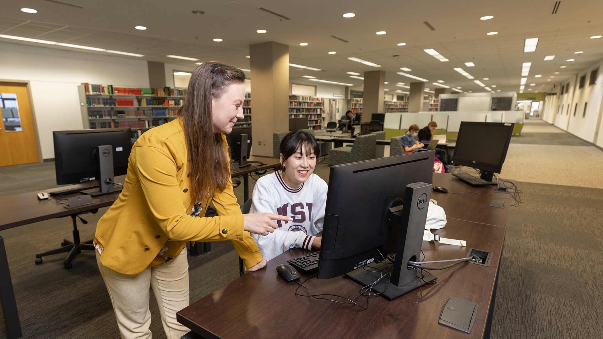 A library worker helping a student at a computer station in Meyer Library.