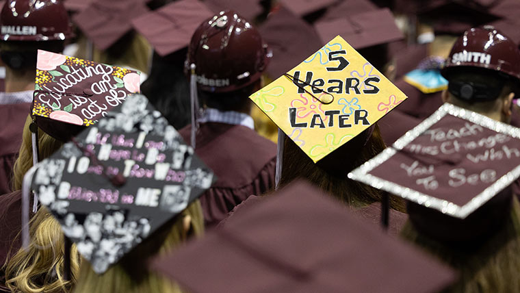 Maroon mortarboards decorated with inspirational teaching messages at commencement.