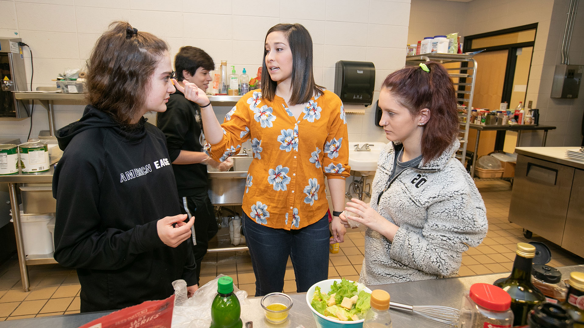 Jordan Belcher, a family and consumer sciences major, advises two students in a kitchen classroom at Republic High School.