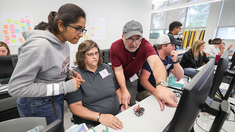 Two people instructing a student during a computer lab exercise.