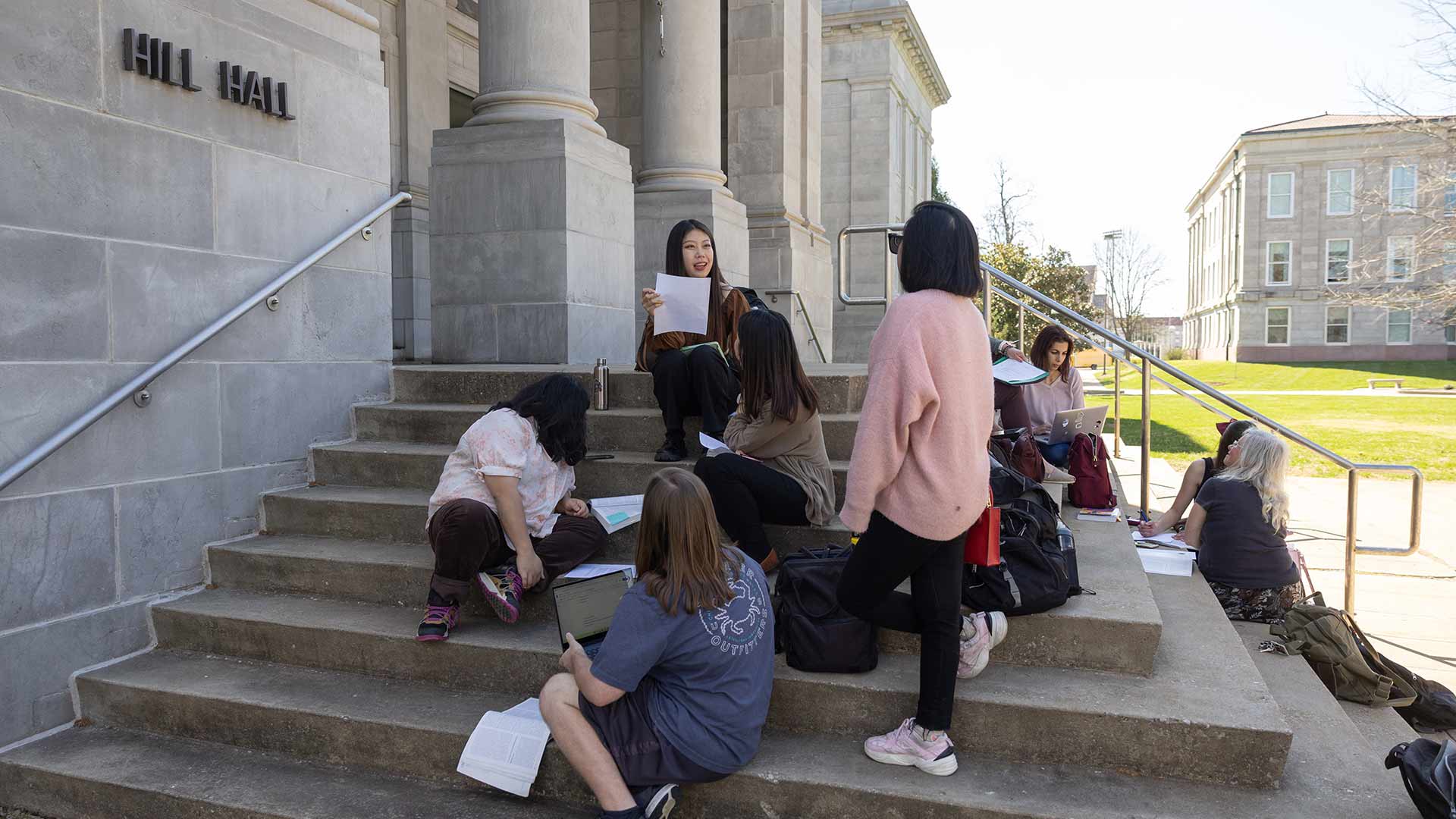 A class studies outside of Hill Hall on a nice day.