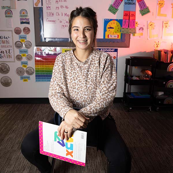 Literacy teacher and Missouri State alum Jennifer Kim seated in a chair and holding a book.