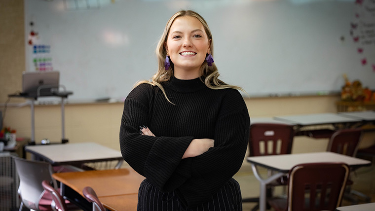 A middle school teacher smiles for a posed photo while alone in the classroom.