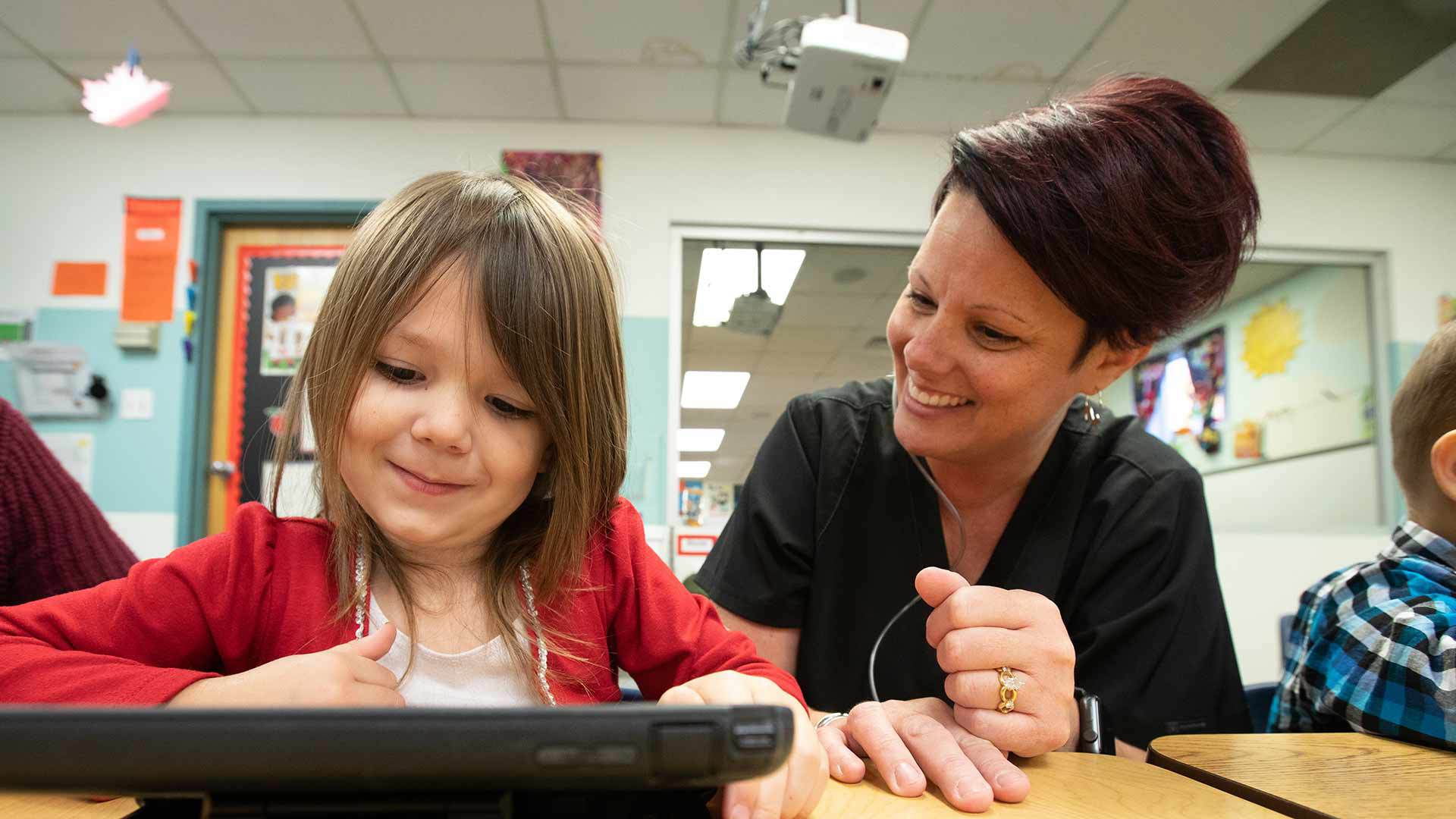 Teacher helping student through course work on tablet.