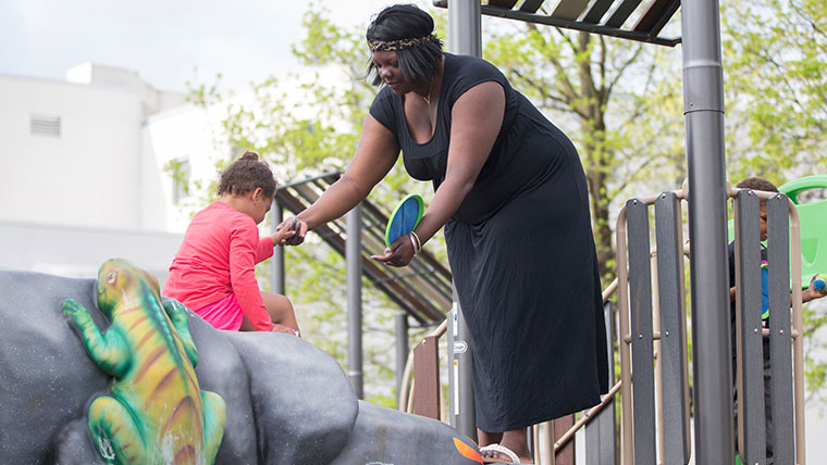 A child care instructor helping a toddler move around on a playset outside.