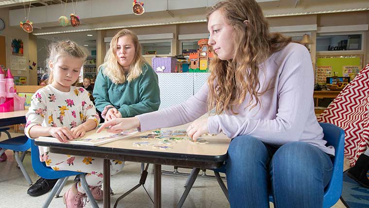 Two child development students and a young girl build a puzzle.