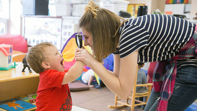 Teacher looking through a magnifying glass at a small child