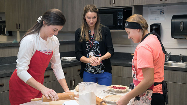 Teacher watching two students make pies in a university kitchen