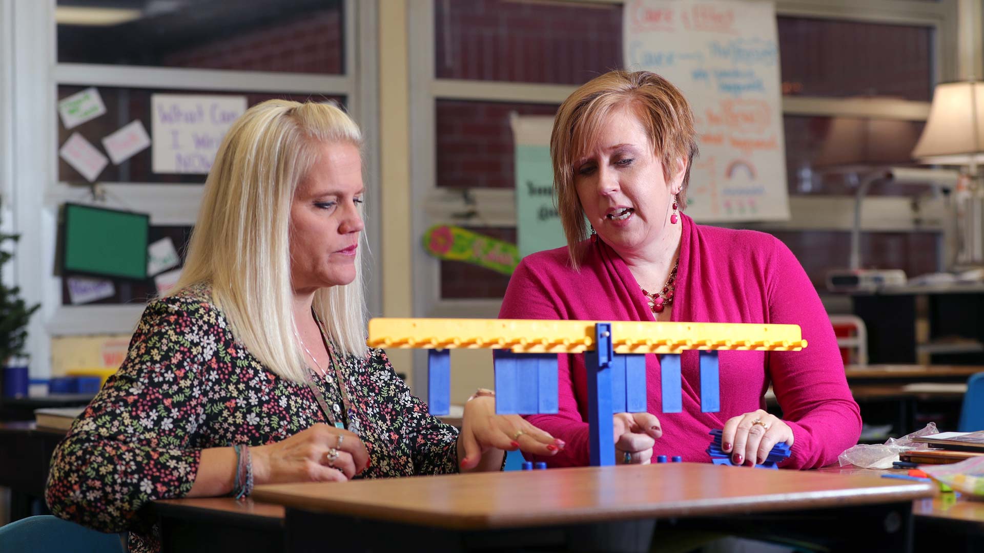 Two individuals sitting at a table within a classroom