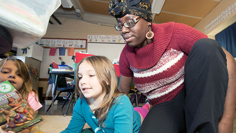 Teacher watching over a child's shoulder as they look at a book.