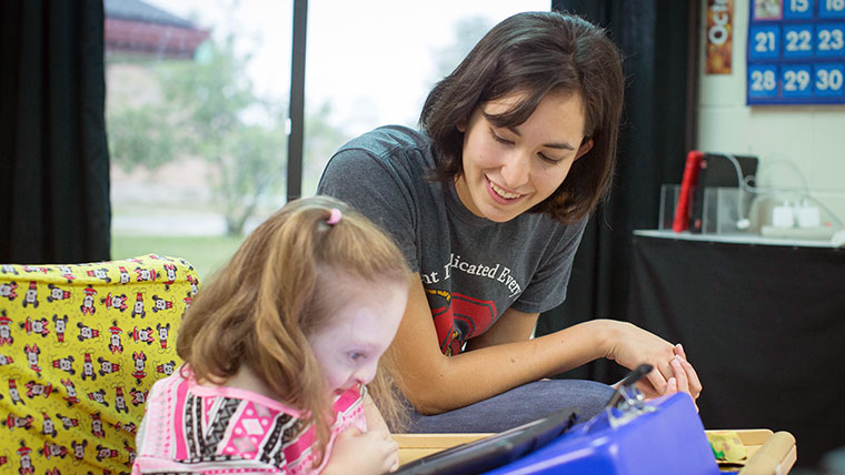 Teacher sitting with a child while they read.