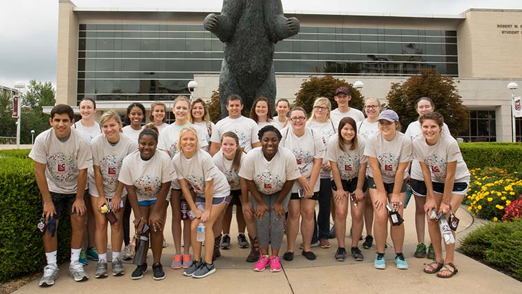 A large group of students from Living-Learning Communities posing in front of the Bear statue by Plaster Student Union.