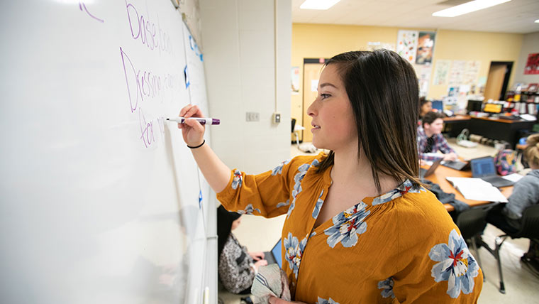 A high school teacher writing on a dry erase board during class.