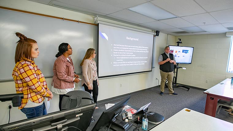 Four students giving a PowerPoint presentation to a class.