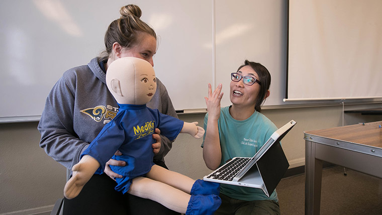 Two students working with a simulation doll in a child behavior class.