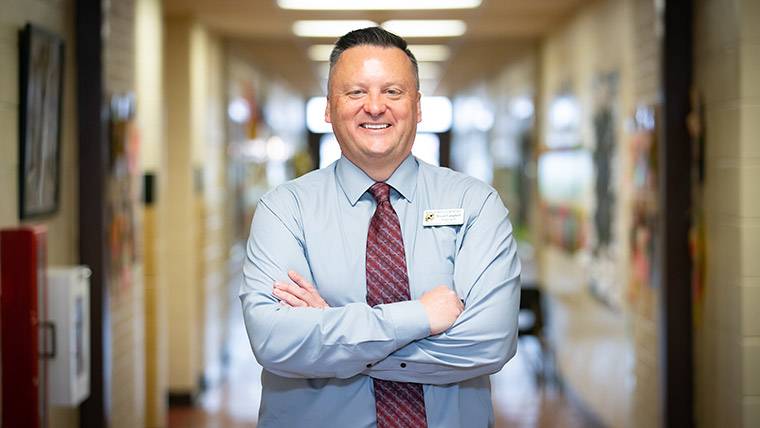 An elementary school principal posing in the hallway of his school.