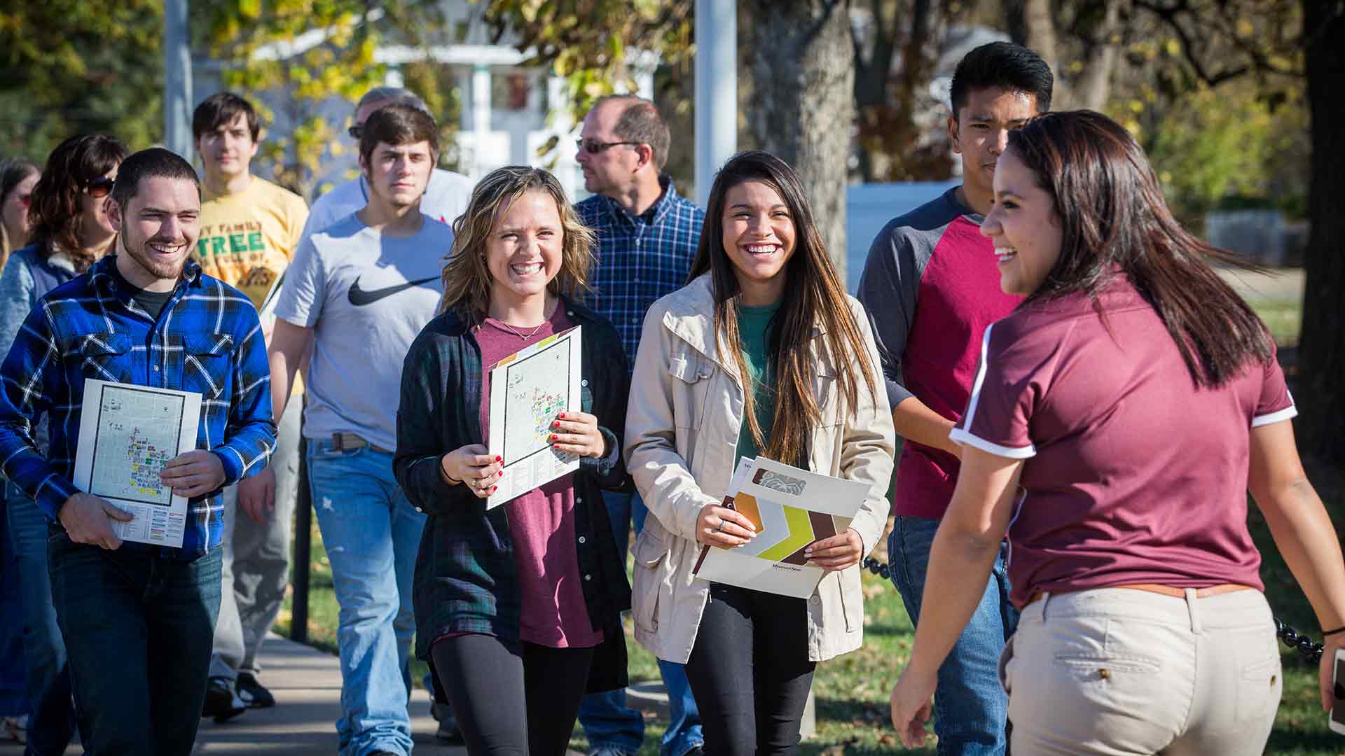 A tour guide leading a group of smiling students and their families on a campus tour.