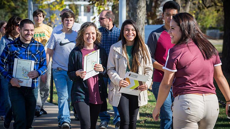 A tour guide leading a group of smiling students and their families on a campus tour.