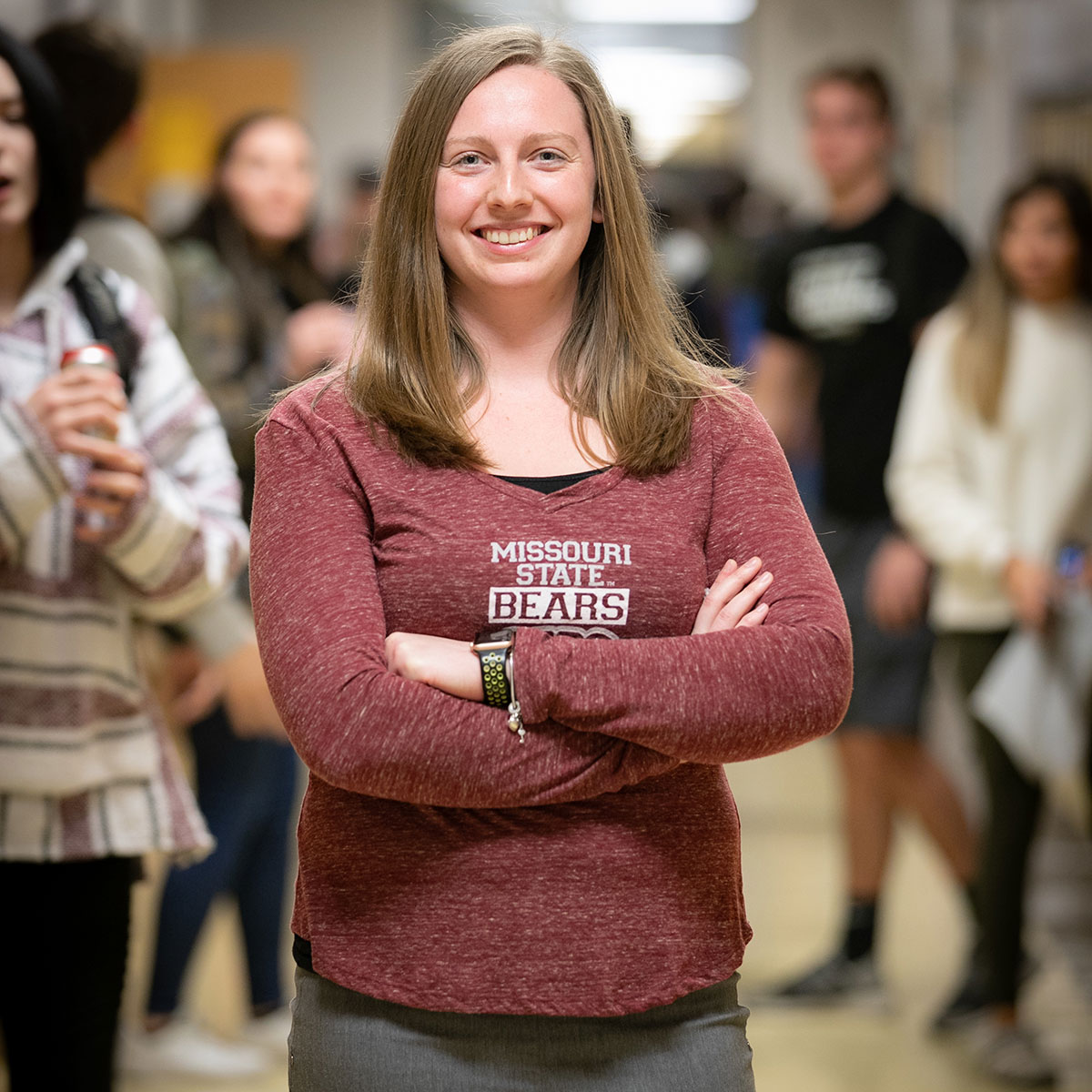 MSU alum Symantha Campbell smiles and stands with her arms crossed in the hallway of Farmington High School.