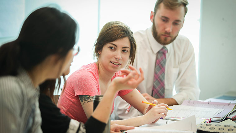 Four students discuss class material with their notes on the table in front of them.