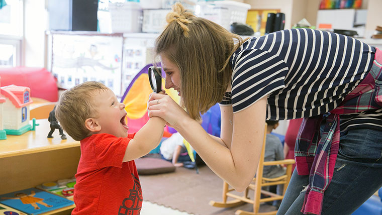 Teacher looking at a smiling toddler through a magnifying glass