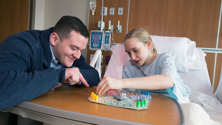 Man playing a board game with a young person in a hospital bed